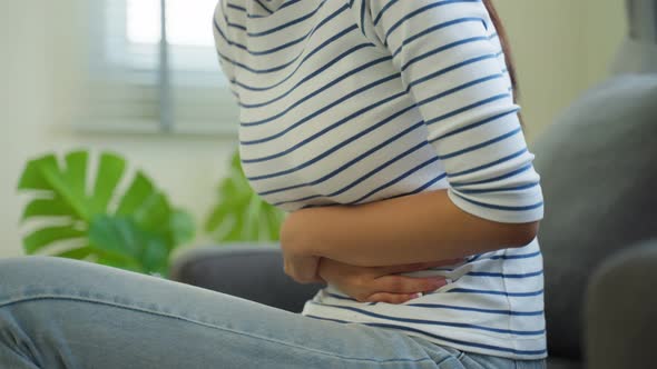 Asian beautiful sick girl suffer from hurt stomachache in living room.