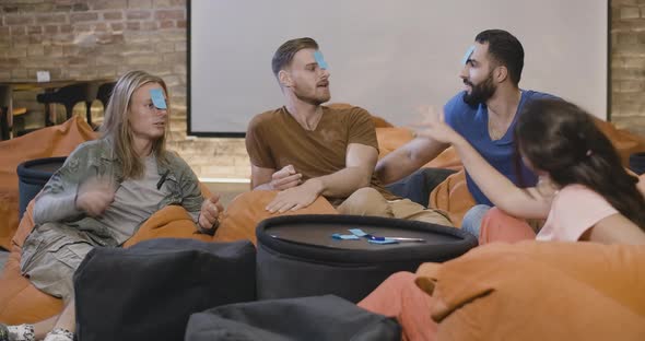 Group of Cheerful Friends Playing Game with Sticky Notes on Foreheads. Young Multiethnic Men and