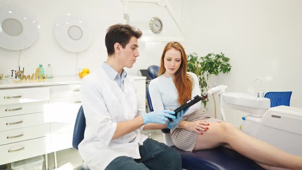 Young Man Dentist Showing Xray on Digital Tablet to Female Patient Sitting in Dental Chair