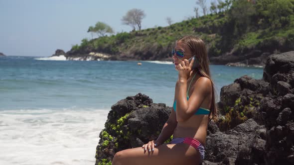 Girl with Cellphone Sits on the Rock and Looks at the Sea