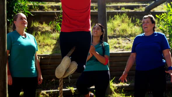 Women applauding female trainer while rope climbing