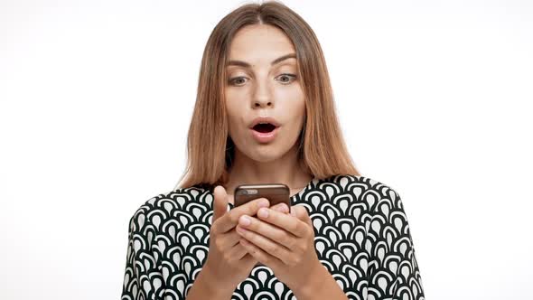 Surprised Young Beautiful Blonde Girl Smiling Looking at Phone Over White Background