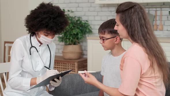 Afro American Woman Doctor in Mask Looking at Child's Body Temperature Reading on Thermometer While