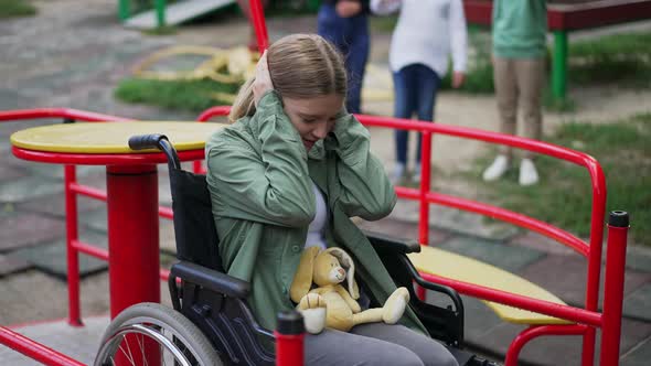 Bullied Caucasian Disabled Girl in Wheelchair Closing Ears Looking at Camera As Unrecognizable