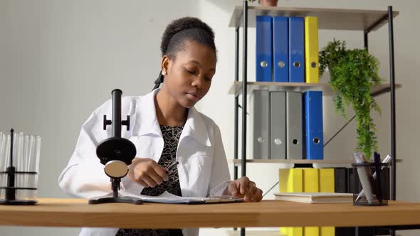 African Female Scientist Doing Some Research and Looking Through a Microscope in Laboratory