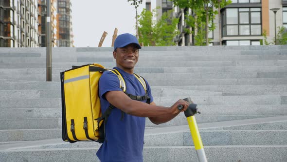 Portrait Smiling Afroamerican Man Courier with Backpack and Electric Scooter