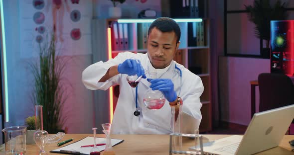 Male Chemist in White Coat Conducting Chemical Experiment with Liquids in Evening Lab