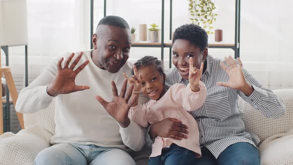 Afro American Happy Family Sitting at Home Sofa Waving Hello Looking at Camera Little Girl Daughter