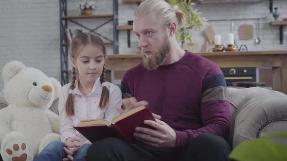 Young Caucasian Man Sitting with Book and Talking To Teenage Girl. Brunette Pretty Daughter Shaking