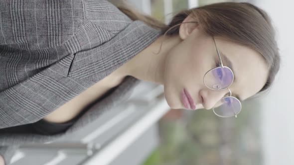 Vertical Video. Beautiful Girl in Glasses and a Gray Suit. Slow Motion