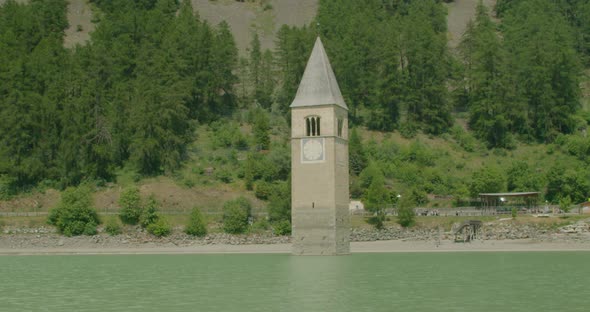 Full shot, scenic view of Kirchturm von Altgraun in Italy, Reschensee shore and forest range in the