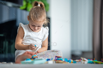 Concentrated Little girl playing with small constructor toy on floor in home, educational game
