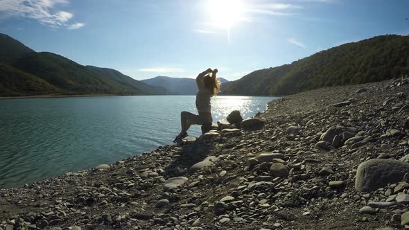 Young Happy Female Sitting on Riverbank in Sunbeams and Stretching, Freedom