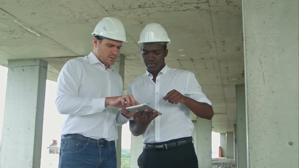 African American Engineer and Caucasine Architect Using Digital Tablet and Wearing Safety Helmets at