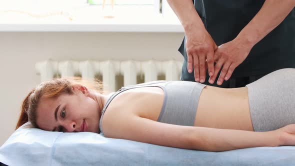 Young Woman at Massage Session - Lying on a Couch - the Massagist Pressing on Her Spine with His