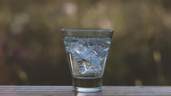 Mineral Water in a Glass with Ice Cubes Stands on the Nature