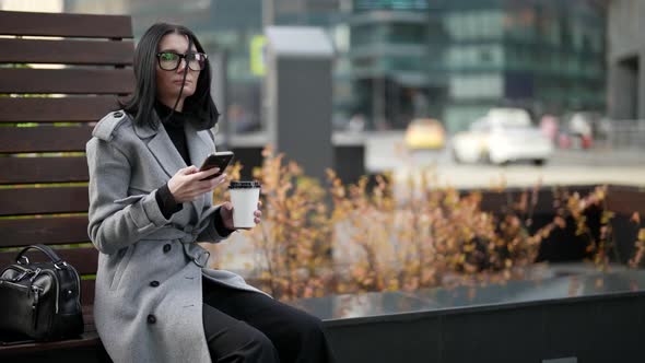 City Life in Downtown Successful Woman is Using Smartphone and Drinking Coffee