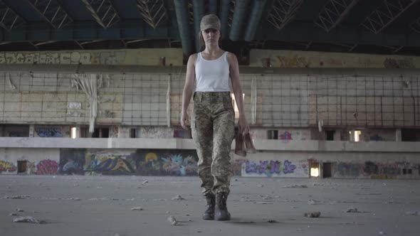 Attractive Young Woman in Military Uniform Walking Slowly in Dusty Dirty Abandoned Building Carrying