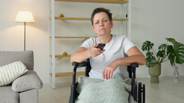Senior Lady in Wheelchair Watching Tv in Living Room Holding Remote Control Changing Tv Channels