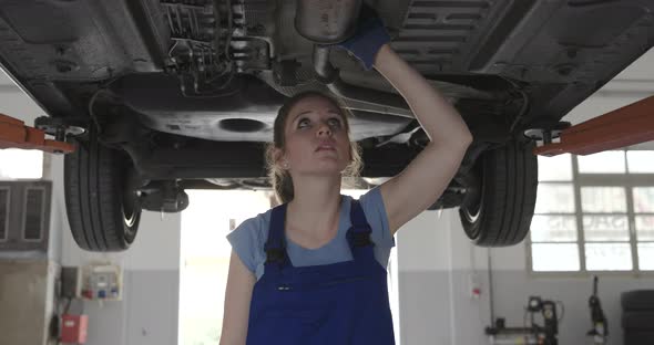 Confident female mechanic in a repair shop, she is working under a car, women's employment concept