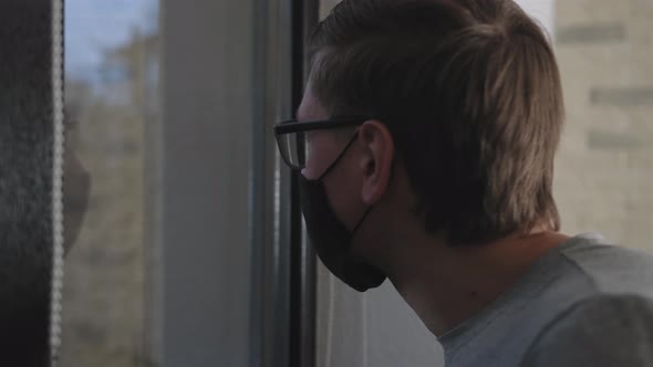 Mman with Medical Mask Looking Out of the Window During Coronavirus Quarantine.