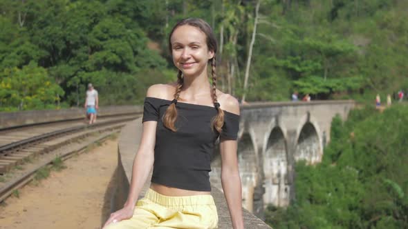 Girl with Braids Sits on Old Bridge Smiling Against Forest