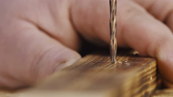 Drill Bit is Attached to Wooden Bar Held By Mans Hand and Begins to Rotate Drilling It Closeup