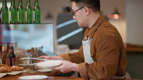 Smiling barista puts a croissant in a plate from the display case