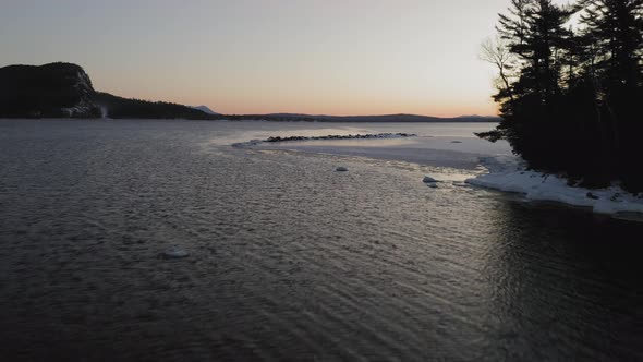 Flying quickly past a small island surrounded by ice at sunrise AERIAL