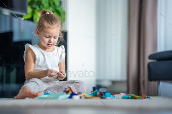 Little girl play with small constructor toy on floor in home living room, educational game, spending