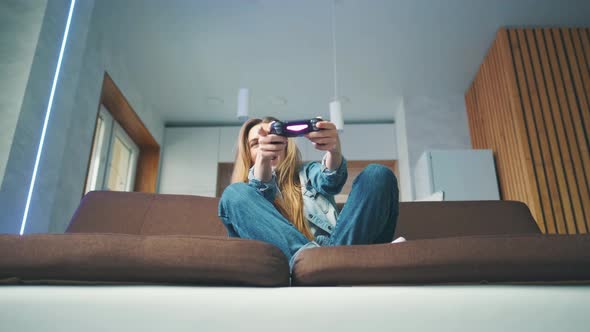 A Beautiful Excited Young Gamer Girl is Sitting on a Couch and Playing Video Games on a Console