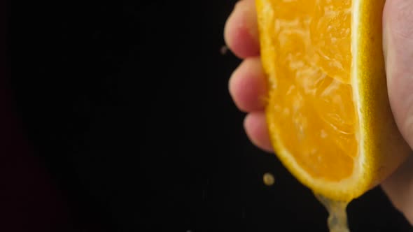 Hand squeezing orange slow motion on black background