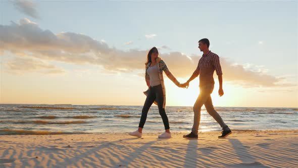 A Loving Couple Walking Holding Hands. Going Along the Seashore at Sunset