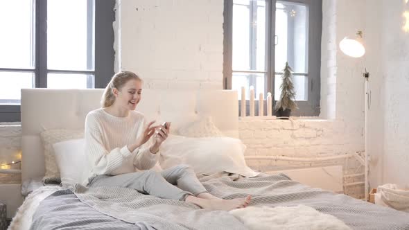 Excited Girl Sitting in Bed Celebrating Success on Smartphone