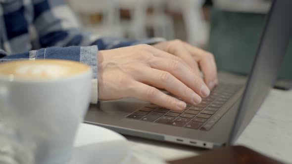 Male Hands Type on Laptop Keyboard in Cafe