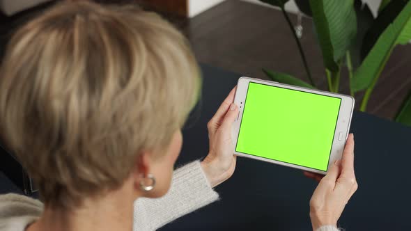A Middleaged Woman is Viewing Content Using a Tablet on a Green Screen