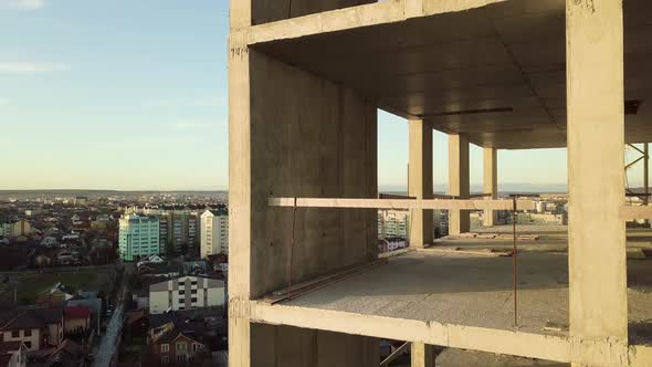 Aerial view of concrete frame of tall unfinished apartment building under construction in a city.