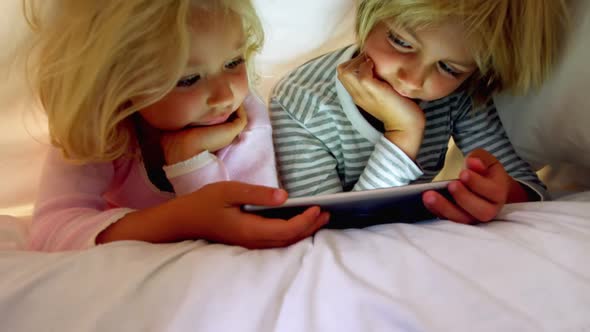 Siblings using digital tablet under blanket in bedroom at home 4k