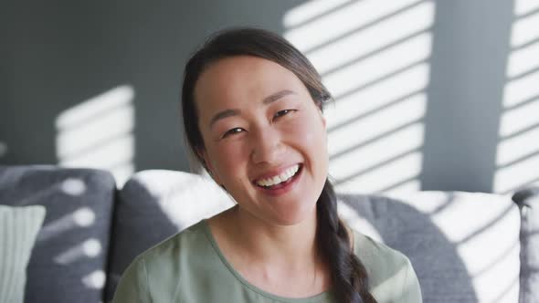 Happy asian woman sitting on sofa close to window at home