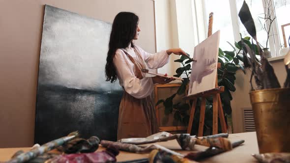 Art Studio  Young Woman Drawing a Purple Painting with Oil Paints