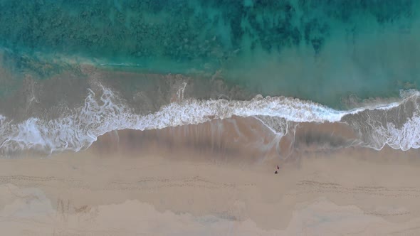 Aerial descending over two people walking on sandy beach and waves breaking on seashore