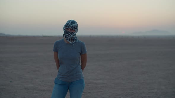 Woman Wearing Checkered Keffiyeh Standing in the Desert Waiting for Sunrise Looking at Camera