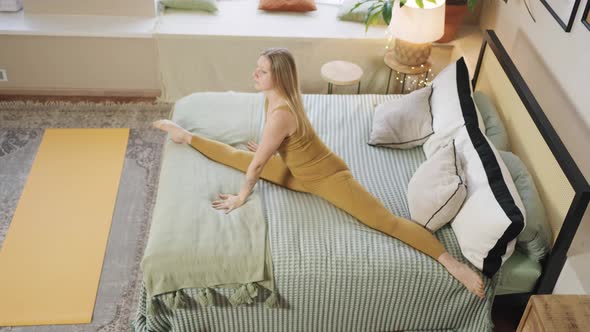 Woman Wearing Sports Outfit Does Split Stretching on Bed