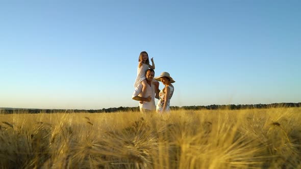 Happy parents and little daughter dancing in wheat field at sunset