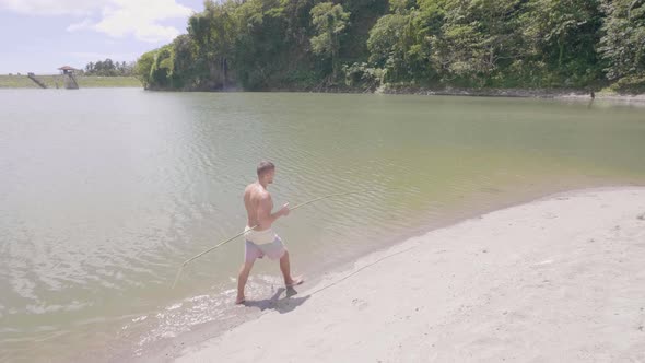 Young Fisherman with Handmade Fishing Rod Walking on Sandy Shore of Tropical Lake. Man with Wooden