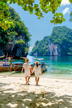 , is a beautiful beach with longtail boats, a couple of European men and an Asian woman on the beach. Couple on a boat trip in Krabi Thailand