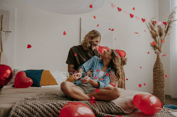 Happy loving couple sitting on bed and throwing heart shape confetti 