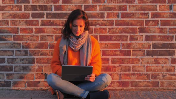 Woman with Laptop Sitting on Floor Near Brick Wall