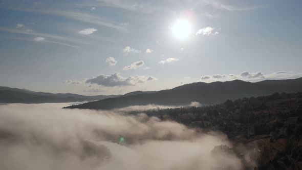 Aerial Drone Flight View Over Low Clouds and Morning Mist Covered Mountain Slopes at Sunrise