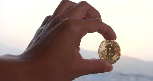 Hand Holding Bitcoin Over the Sunset Time